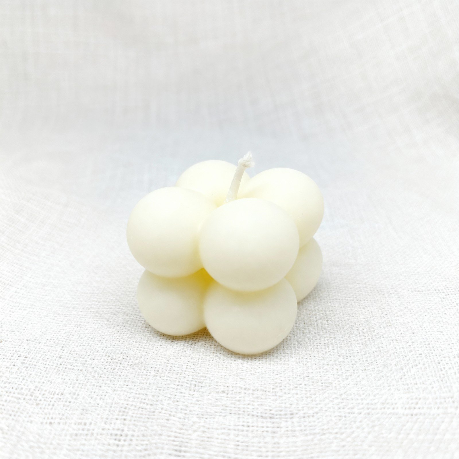 Minimal bubble candle made of smooth rounded spheres, placed on a neutral fabric background.