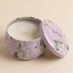 A round, bulbous metal candle tin featuring a pastel lavender background with a white rose floral pattern. The lid, leaning against the side, features the text