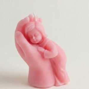 A pink, sculptural wax candle depicting a large hand gently cradling a small, sleeping child, symbolizing protection, comfort, and care against a plain white background.
