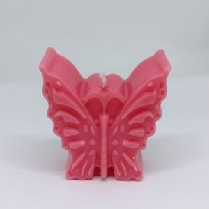 A close up of a bright pink, butterfly-shaped decorative candle standing upright on a white background. The candle features detailed molded wings with small circular patterns and ridges, and a white wick at the top center.