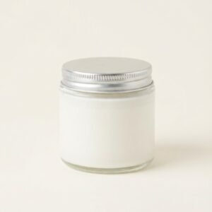 A close up shot of a small, clear glass jar candle with a silver screw-top lid and smooth white wax. The jar is centered on a plain white background, representing a minimalist product of Lunis Candles.