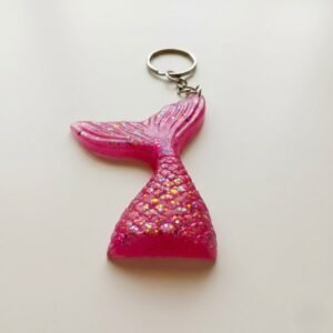 A handcrafted bright pink mermaid tail keychain by Lunis Resin Art lying flat on a white background. The keychain is made of glossy epoxy resin filled with multicolored holographic chunky glitter. It is attached to a silver metal chain and split ring.