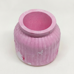 A small blush tinted concrete pot with vertical ribbed texture and a smooth round opening, handcrafted in a minimalist style.