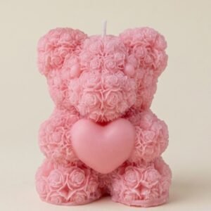 A bright pink, highly textured scented candle shaped like a teddy bear sitting down and holding a smooth heart. The bear's surface is detailed with tiny, densely packed rose shapes.