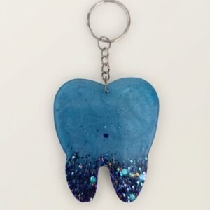 A handmade, tooth shaped resin keychain by Lunis Resin Art. The top part is a solid, shimmering teal blue, and the roots feature a dark blue/purple ombre filled with chunky, holographic glitter.