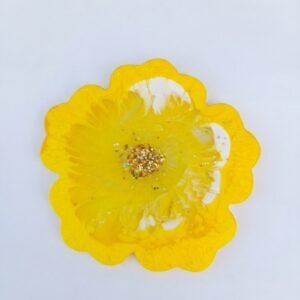 A bright, flower shaped resin coaster or small tray in a vibrant yellow color with white swirl accents and a cluster of gold glitter in the center.