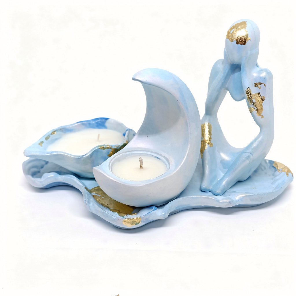 A light blue and gold leaf ceramic candle holder set featuring a figurine in a thoughtful "Thinker" pose and two embedded candle cups: one shaped like a crescent moon and another like a seashell or leaf, all resting on a matching tray.