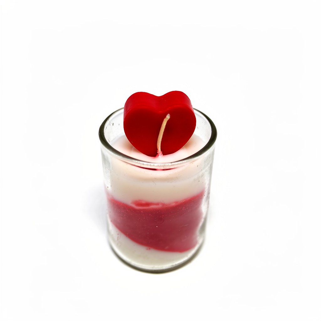 ● A red and white scented candle in a clear glass votive holder. The wax features a diagonal swirl pattern, and the candle is topped with a small, separate red wax heart shape with a wick.