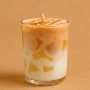A layered soy candle in a glass, featuring creamy white and caramel brown hues with embedded translucent chunks, set on a textured white surface.