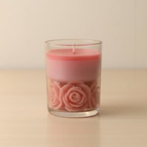 A pink soy candle in a glass by lunis candle, featuring a top layer of smooth pink wax and a bottom layer adorned with embedded rose shaped wax decorations, set on a light textured surface