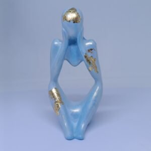 A minimalist blue concrete figurine in a thinking pose with gold foil accents on the head, arm, and leg, displayed against a light background.