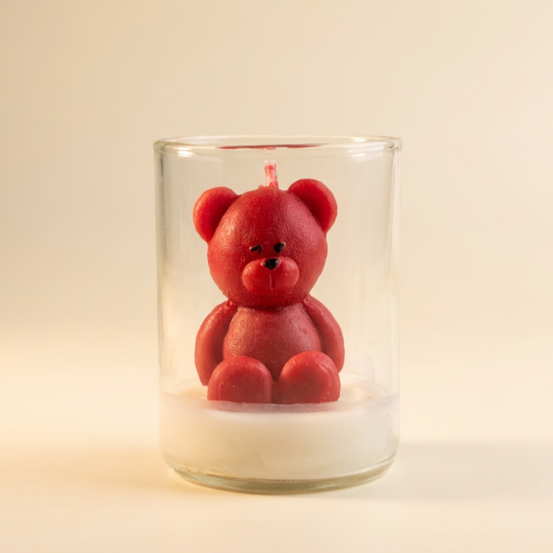 Red teddy bear candle inside a clear glass jar with white wax base.