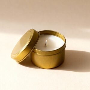 Gold metal tin candle with white wax and open lid on a plain background.