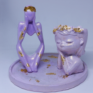 A pastel lavender concrete art set featuring an abstract sitting figure and a serene childlike sculpture, both accented with gold leaf, displayed on a matching round base.