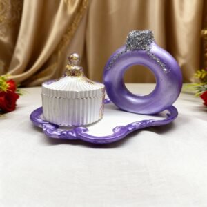 A three piece resin decor set featuring a metallic purple circular donut vase heavily decorated with silver glitter and a fluted white and gold lidded box both sitting on a small ornate purple tray.